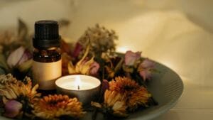 A small brown glass bottle with a black cap and blank label sits on a plate surrounded by dried flowers. A lit tealight candle glows beside it, creating a cosy ambience—perfect as one of your mindfulness gifts for mindful living.