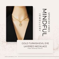 A mannequin wears a gold layered Turkish evil eye necklace with a hamsa hand pendant and three teardrop charms, paired with a black blazer. Text reads: “Gold Turkish Evil Eye Layered Necklace—Triple Teardrop Charms.”.