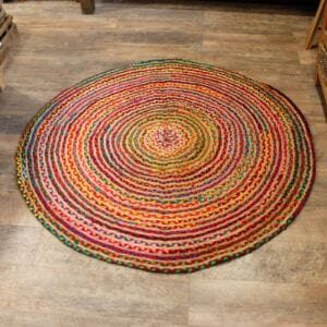 The Round Jute and Recycled Cotton Rug - 150 cm features concentric circles in red, yellow, green, blue, and orange. Its multicolored yarn and slightly uneven edge add charm to any light wooden floor with a lively pattern.