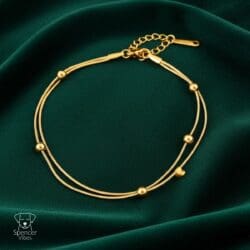The Gold Bead Chain Bracelet – Minimal Adjustable Design features dual thin chains with five gold beads, shown on dark green velvet. An adjustable clasp and the Spencer Vibes logo with a dog illustration are in the lower left corner.