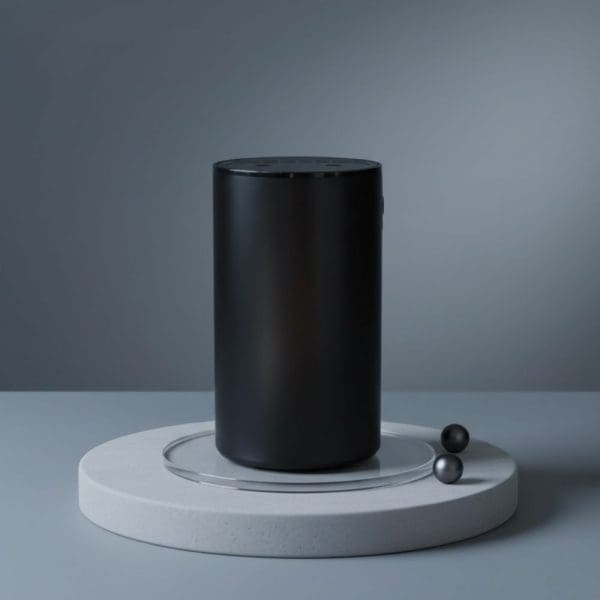 The Essential Oil Diffuser – Waterless Nebuliser USB-C stands upright on a round white platform with a glass ring, flanked by two small black spheres. The background’s smooth grey gradient creates a minimalist, modern display. Includes Free Lavender 10ml & 15% Off Massage Oil.