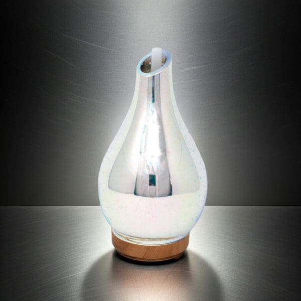 The Infinity Mirror Aroma Diffuser – 3D LED Effect (USB) features a pear-shaped, glass body with a pearlescent finish and sits on a round wooden base, emitting soft white 3D LED light that gently illuminates its metallic, brushed-steel background.