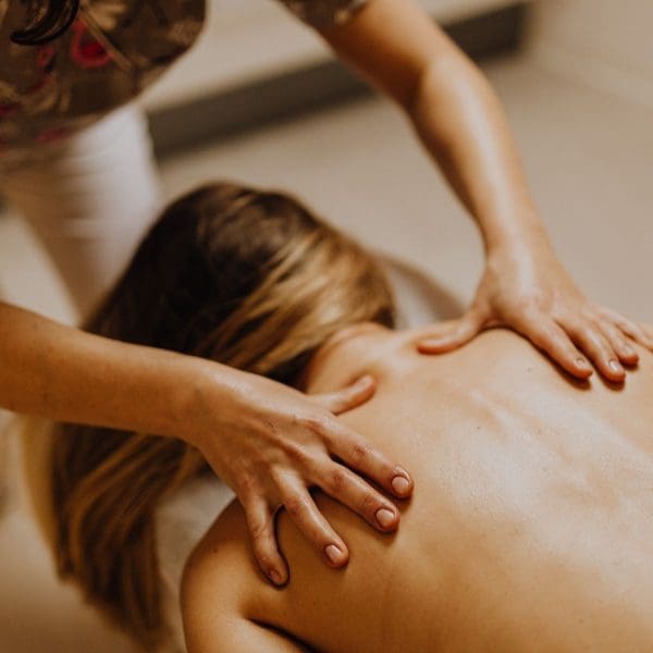 A person with long blonde hair lies face down on a massage table, receiving a back massage from another person. Part of the massage collection, the calm setting features warm lighting as the masseuse’s hands apply soothing pressure to the upper back and shoulders.