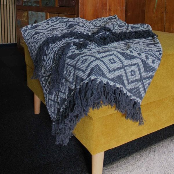 A Boho Comfort Throw with fringed edges draped over a sofa.